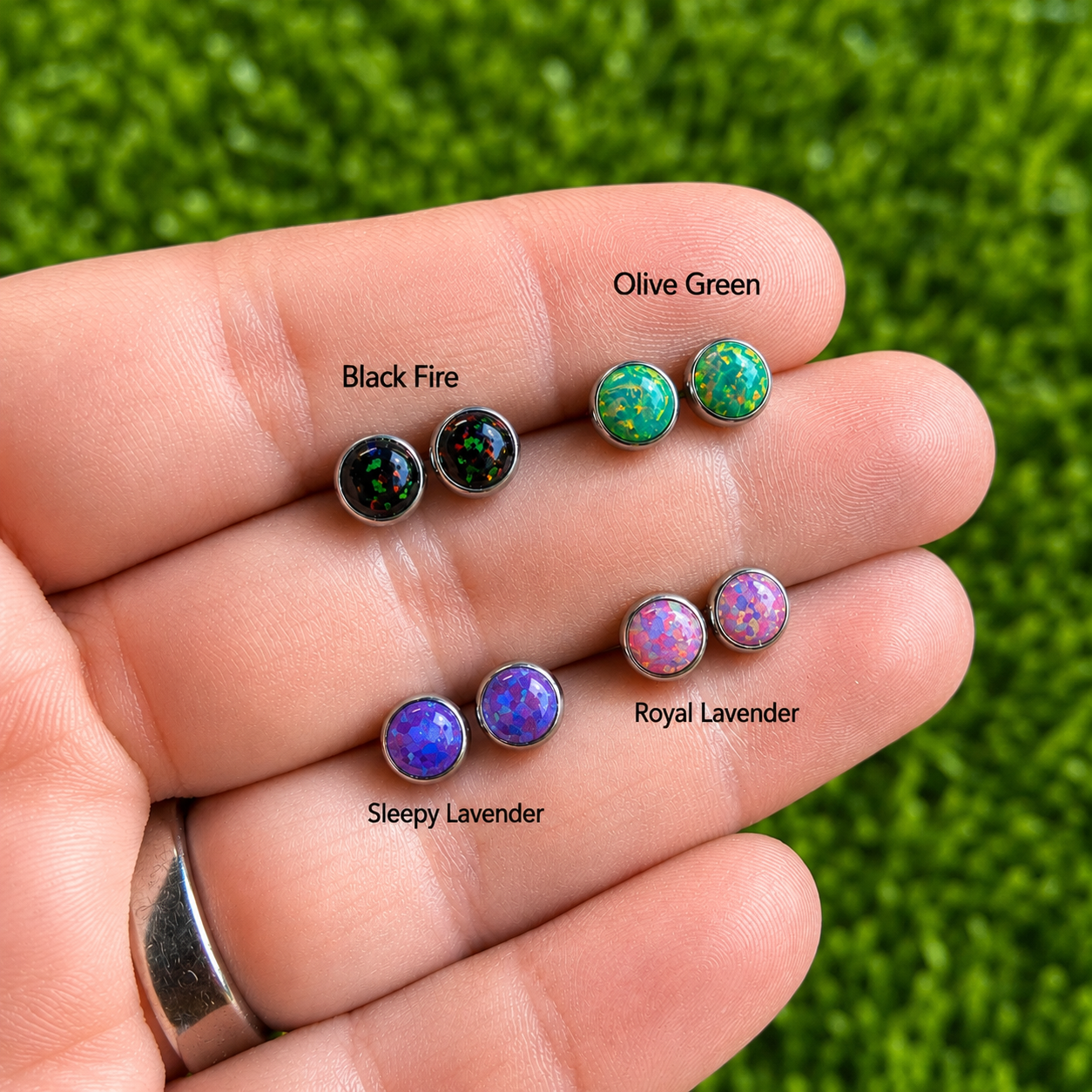 Set of colorful opal stud earrings on a hand with labeled colors against a green grass background.
