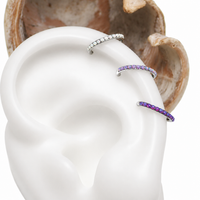 Close-up of an ear with OPAL silver ear cuffs featuring purple gemstones, against a neutral background.
