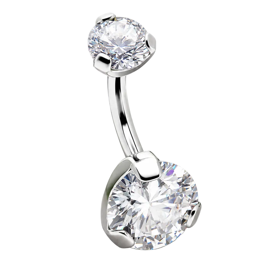 Silver belly button ring with clear gemstones on a stone surface with green leaves in the background