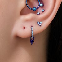 Close-up of an ear with multiple earrings including a blue arrow-shaped earring.