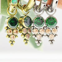 Assorted emerald-colored CZ charms on titanium body jewelry by Body Clickers, showcasing hypoallergenic, colorful decorative accessories.