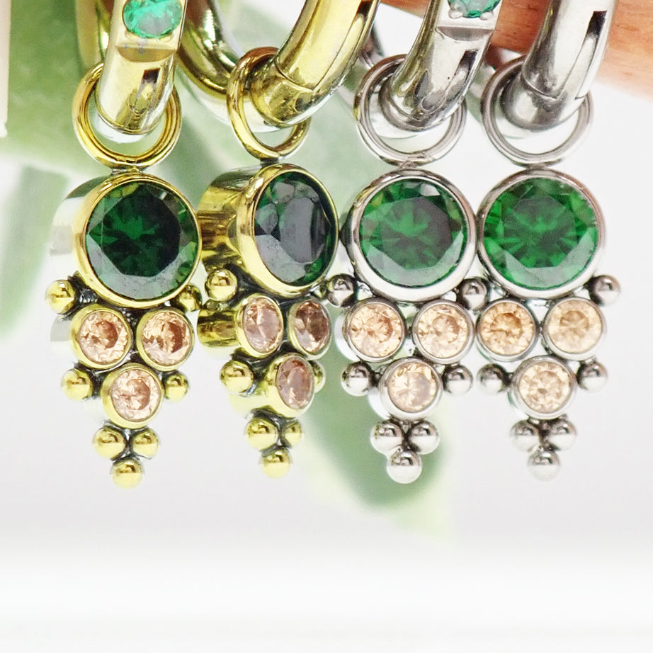 Assorted emerald-colored CZ charms on titanium body jewelry by Body Clickers, showcasing hypoallergenic, colorful decorative accessories.