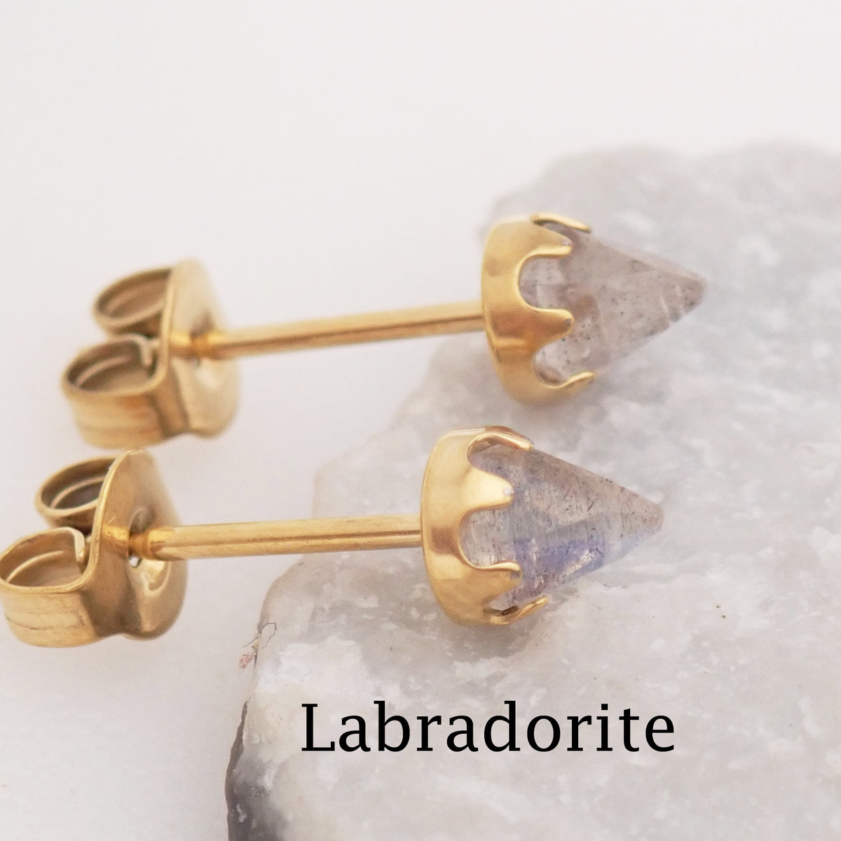 Pair of gold labradorite earrings displayed leaned against a stone with the stone type labeled at the bottom