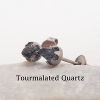 A pair of tourmalated quarts silver cone earrings resting against a stone with a white background