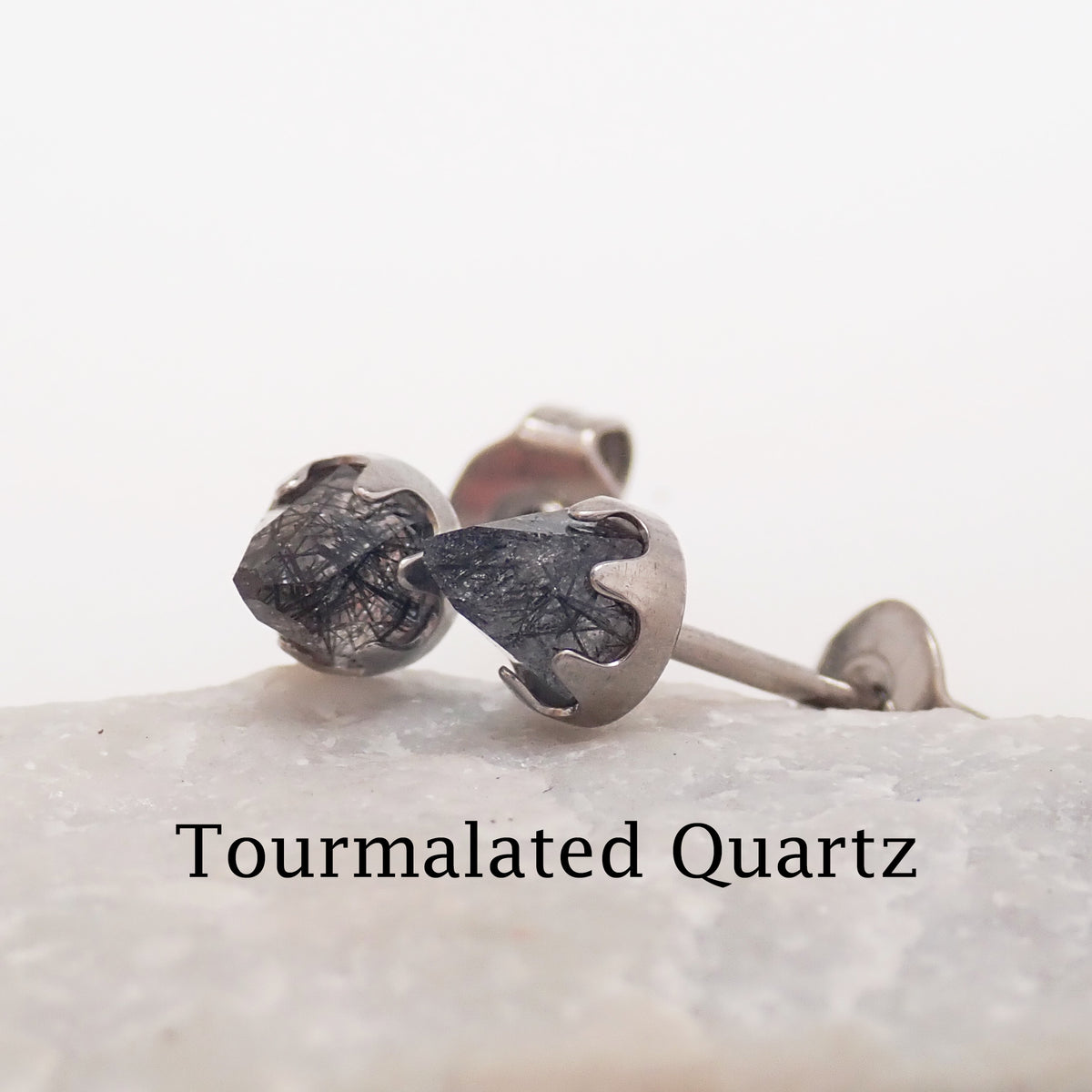 A pair of tourmalated quarts silver cone earrings resting against a stone with a white background