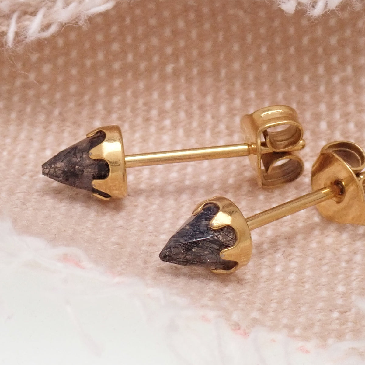 A pair of gold tourmalated quartz cone earrings sitting on a fabric background 