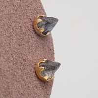 A pair of gold tourmalated quartz cone earrings on a brown display