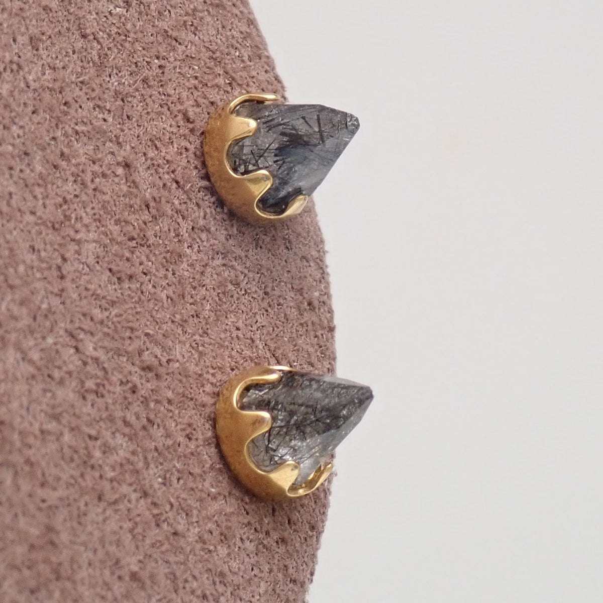 A pair of gold tourmalated quartz cone earrings on a brown display