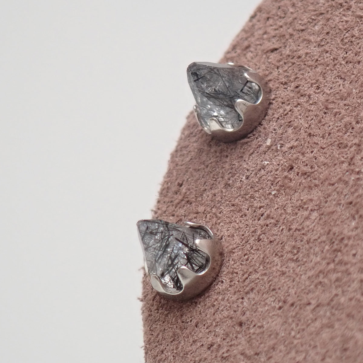 A  pair of silver tourmalated quartz cone earrings on a brown display