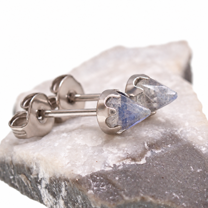 A pair of silver labradorite earrings displayed on a stone 