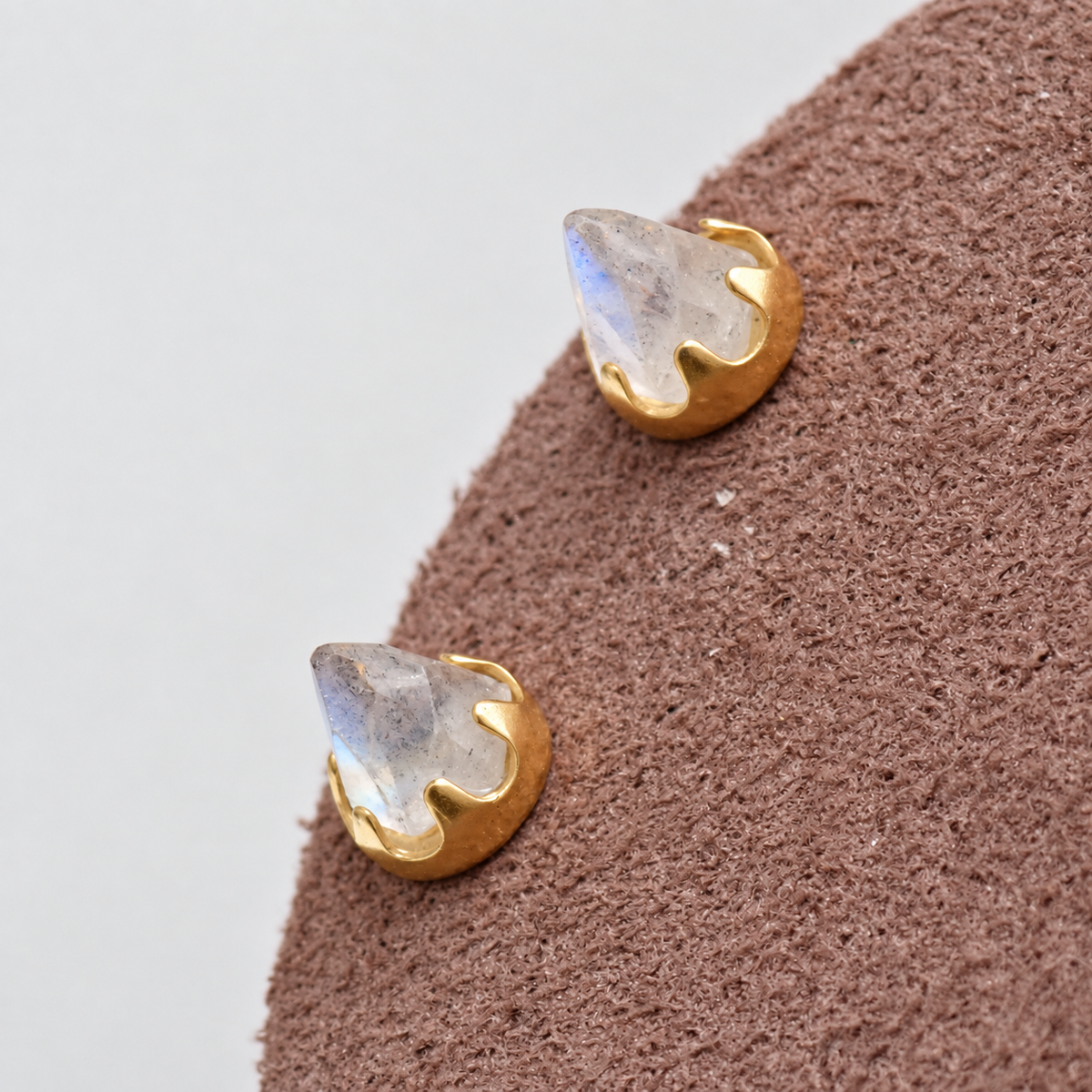 Pair of gold labradorite earrings on a brown display 