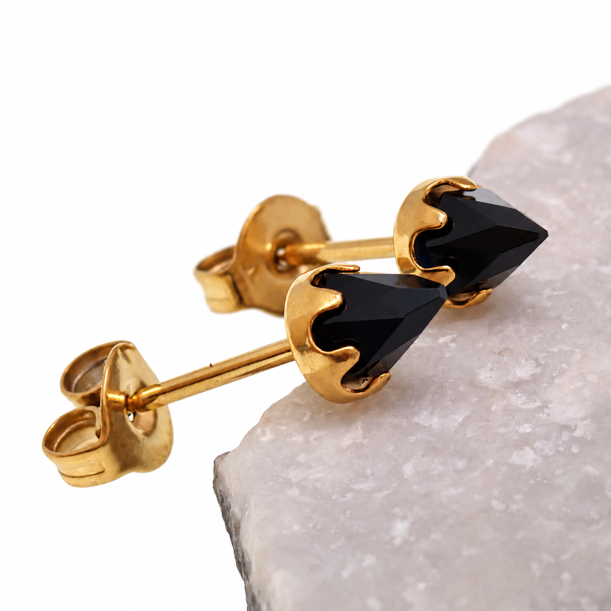 Pair of gold onyx cone earrings leaned against a stone with a white background 