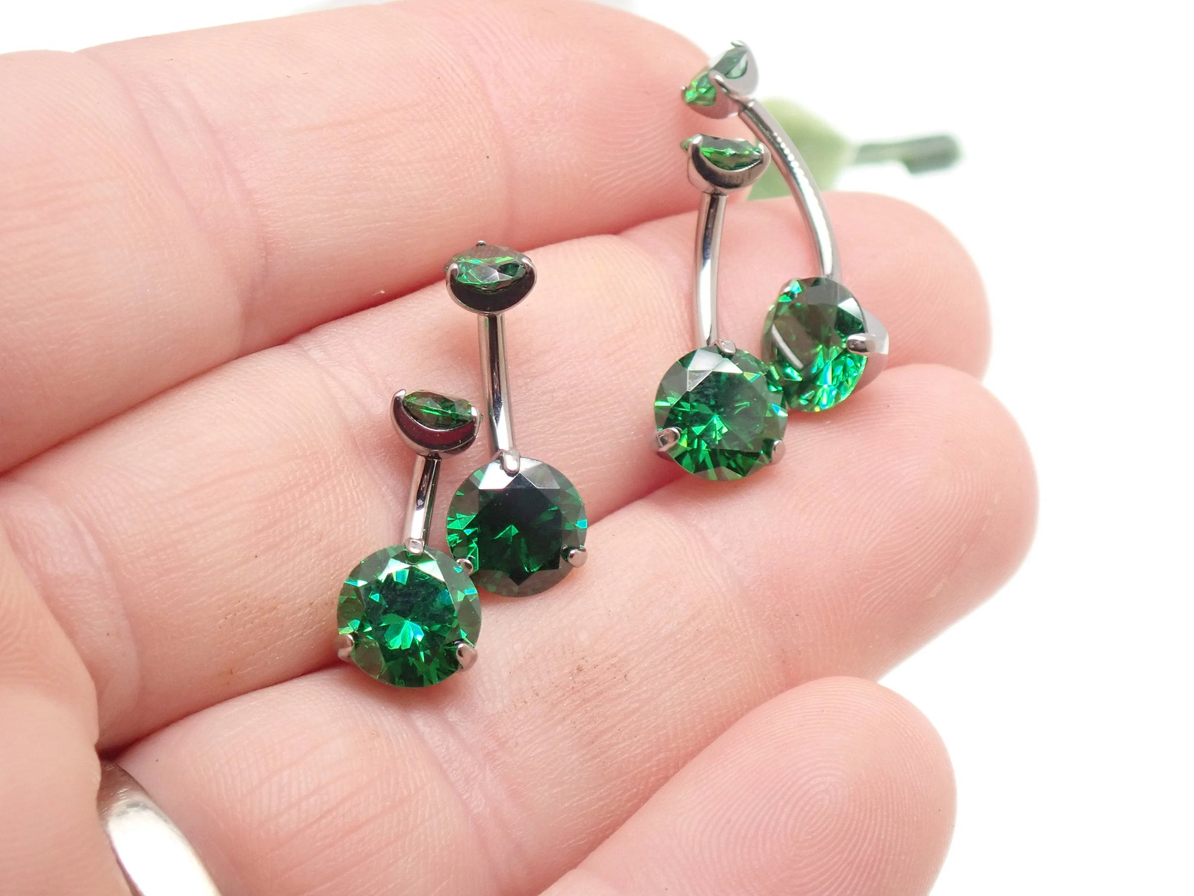 Emerald green CZ prong belly ring in 14g body jewelry held in hand, featuring sparkling cubic zirconia stones.