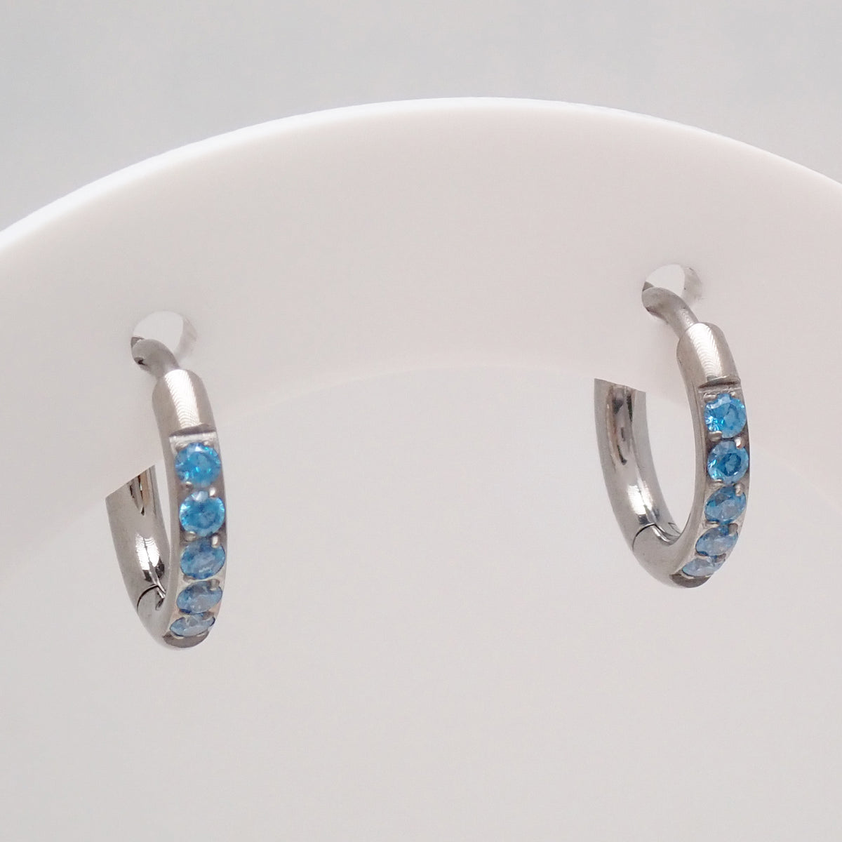 Titanium Hoop earrings with blue CZ on a white display