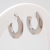 Silver titanium Implant Silhouette Huggie Earrings with hinged clicker closure, 10mm diameter, displayed on stand.