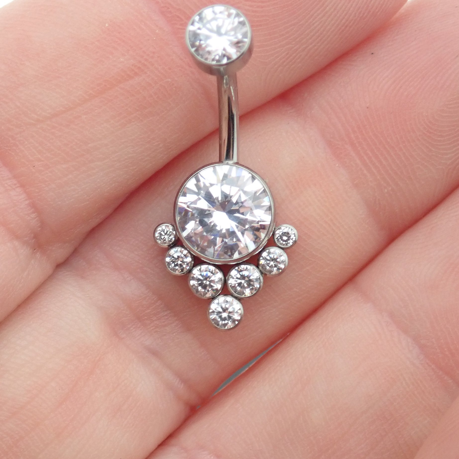 Magpie CZ titanium belly ring, 10mm to 12mm, featuring sparkling stones and a sleek curved design on a hand.