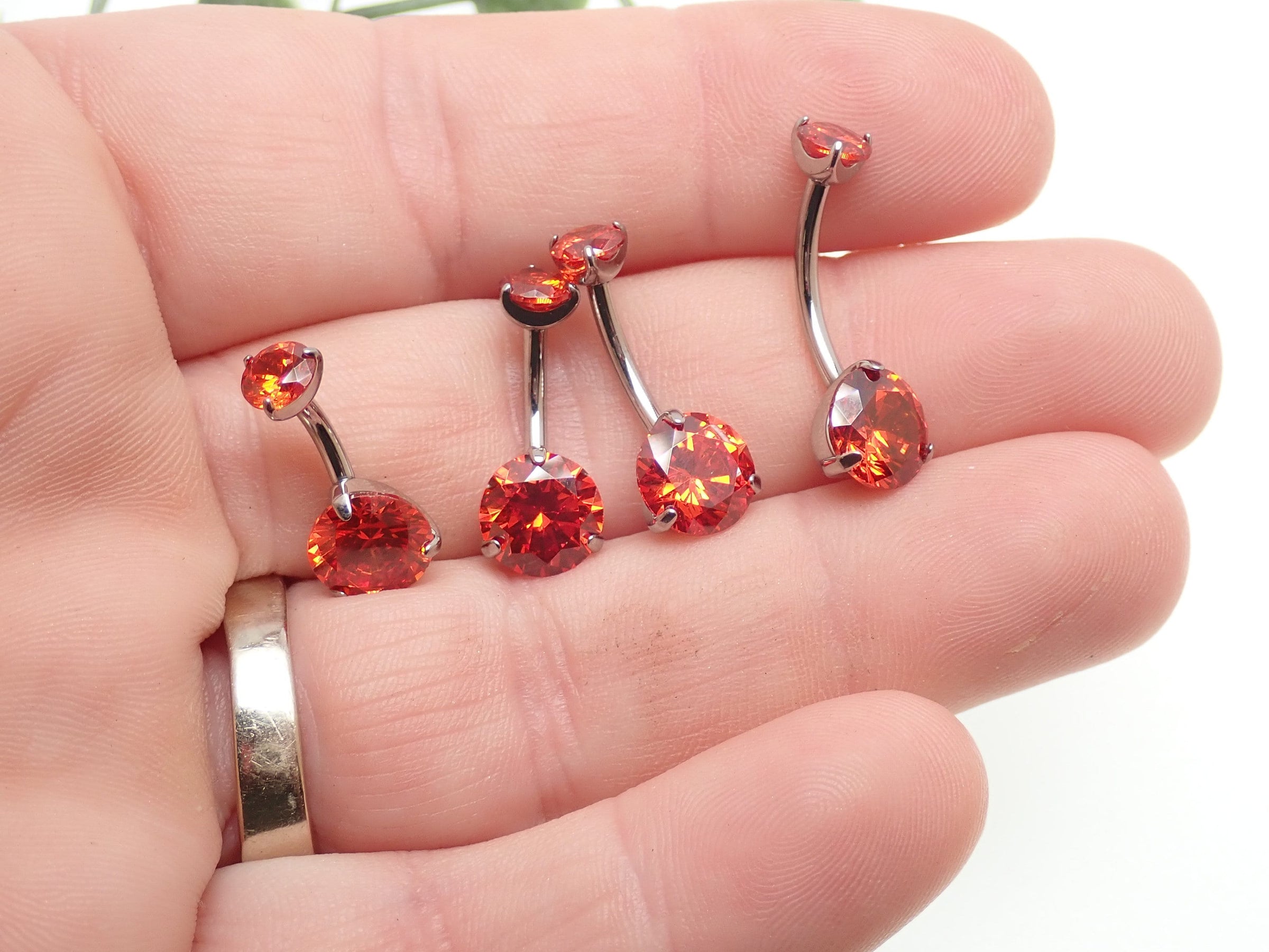Red cubic zirconia prong belly ring from Body Clickers Body Jewelry held in hand, showcasing 14g body jewelry for belly piercing.