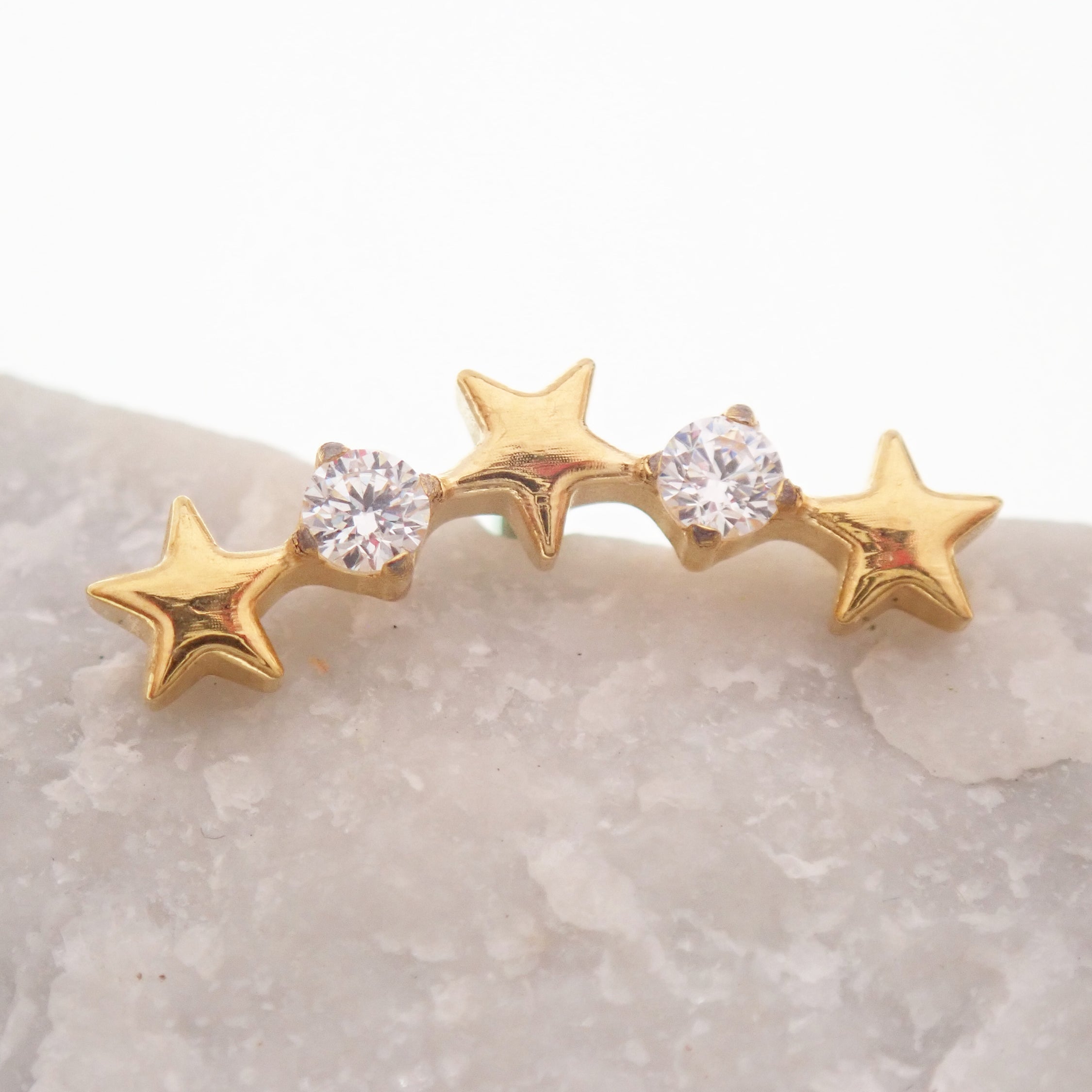 Star CZ PVD Gold Helix Curve titanium flatback labret piercing earrings on a rock, showcasing their elegant star design and gold finish.