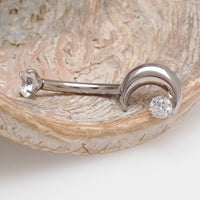 A silver crescent moon belly piercing on a wooden display with a white background 