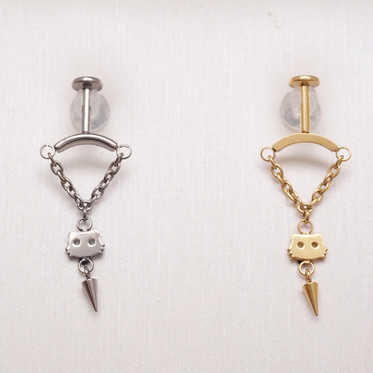 vertical helixpiercing jewelry with chains draping to a cat silhouette with a cone charm under, all on a textured white background
