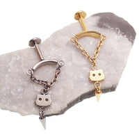 Dangly vertical helix piercing jewelry in silver and gold, sitting on a rock with a white background 
