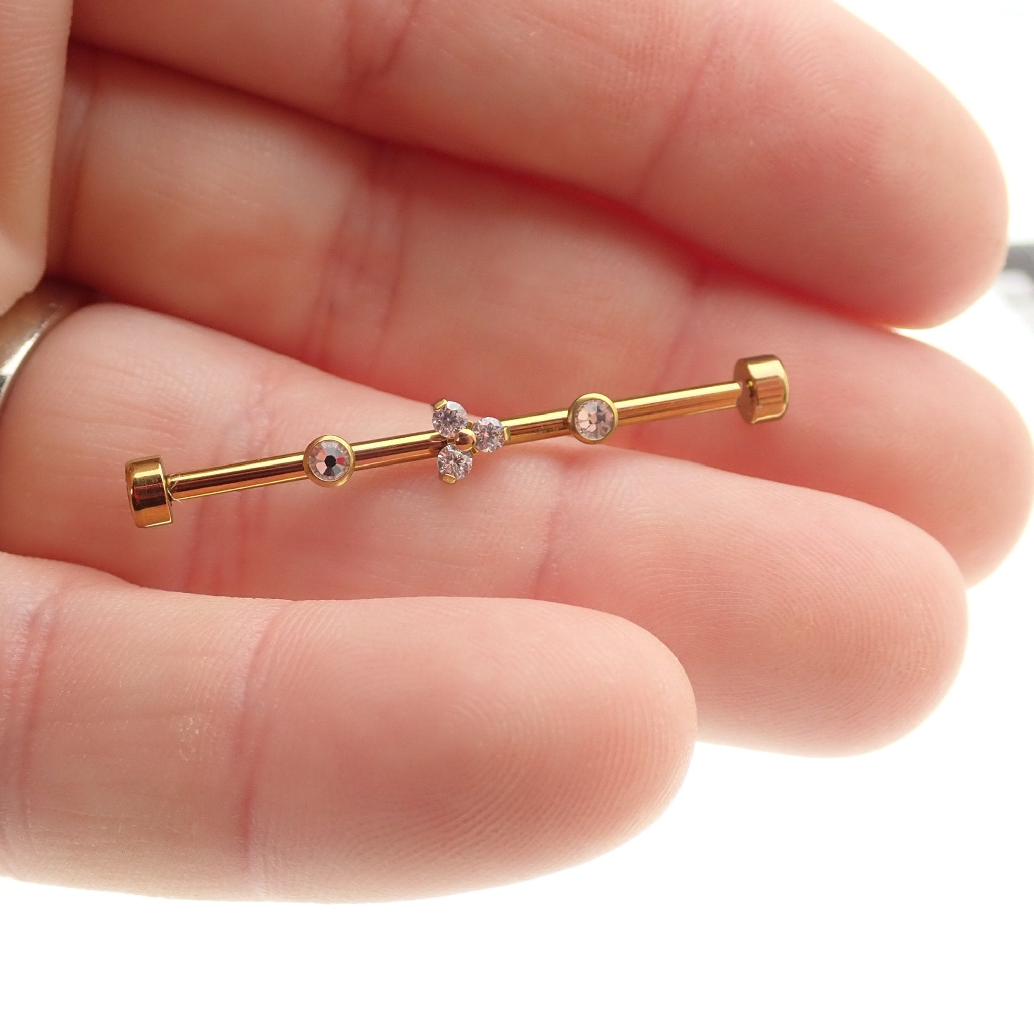 Gold industrial scaffold piercing with clear CZ and Trinity stones, featuring tri-flower design and titanium bar in 14g size.