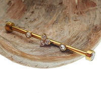 Gold industrial scaffold piercing with clear CZ and Trinity stones, featuring tri-flower design and titanium bar, 14g.