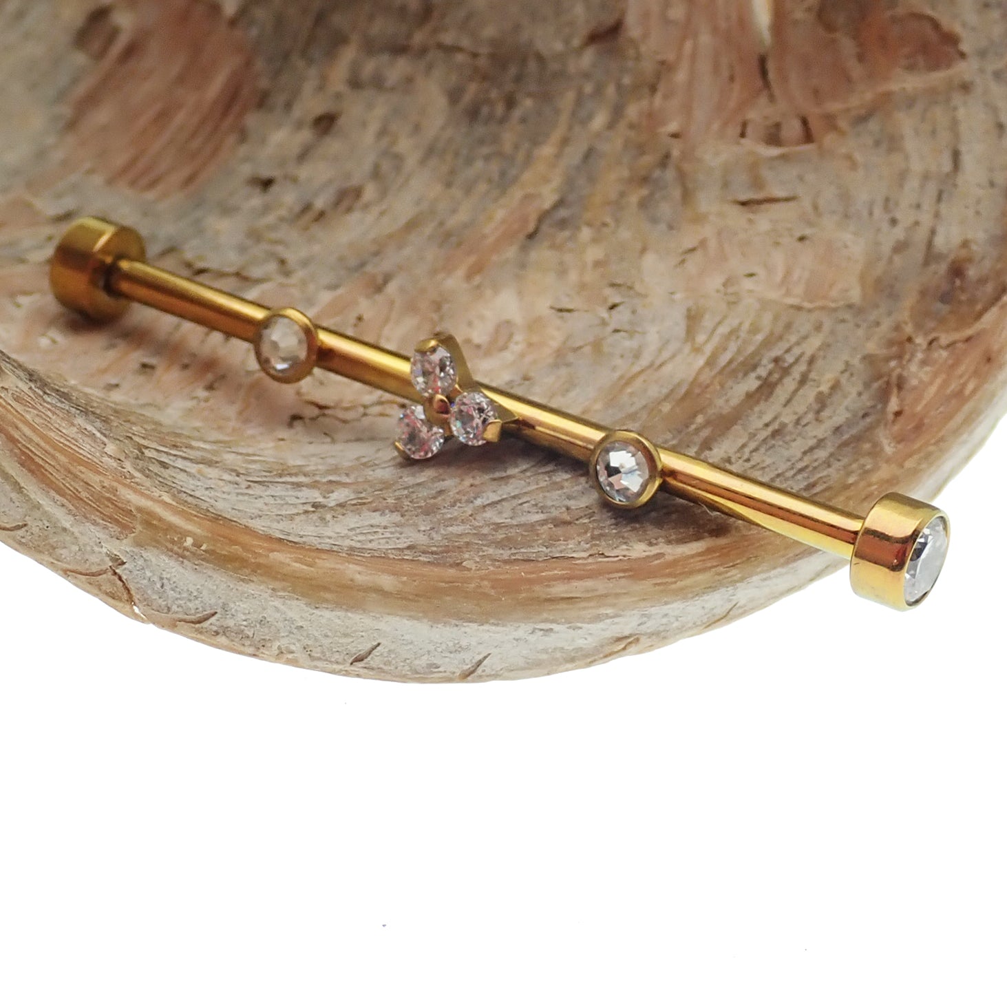 Gold industrial scaffold piercing with clear CZ and Trinity stones, featuring tri-flower design and titanium bar, 14g.