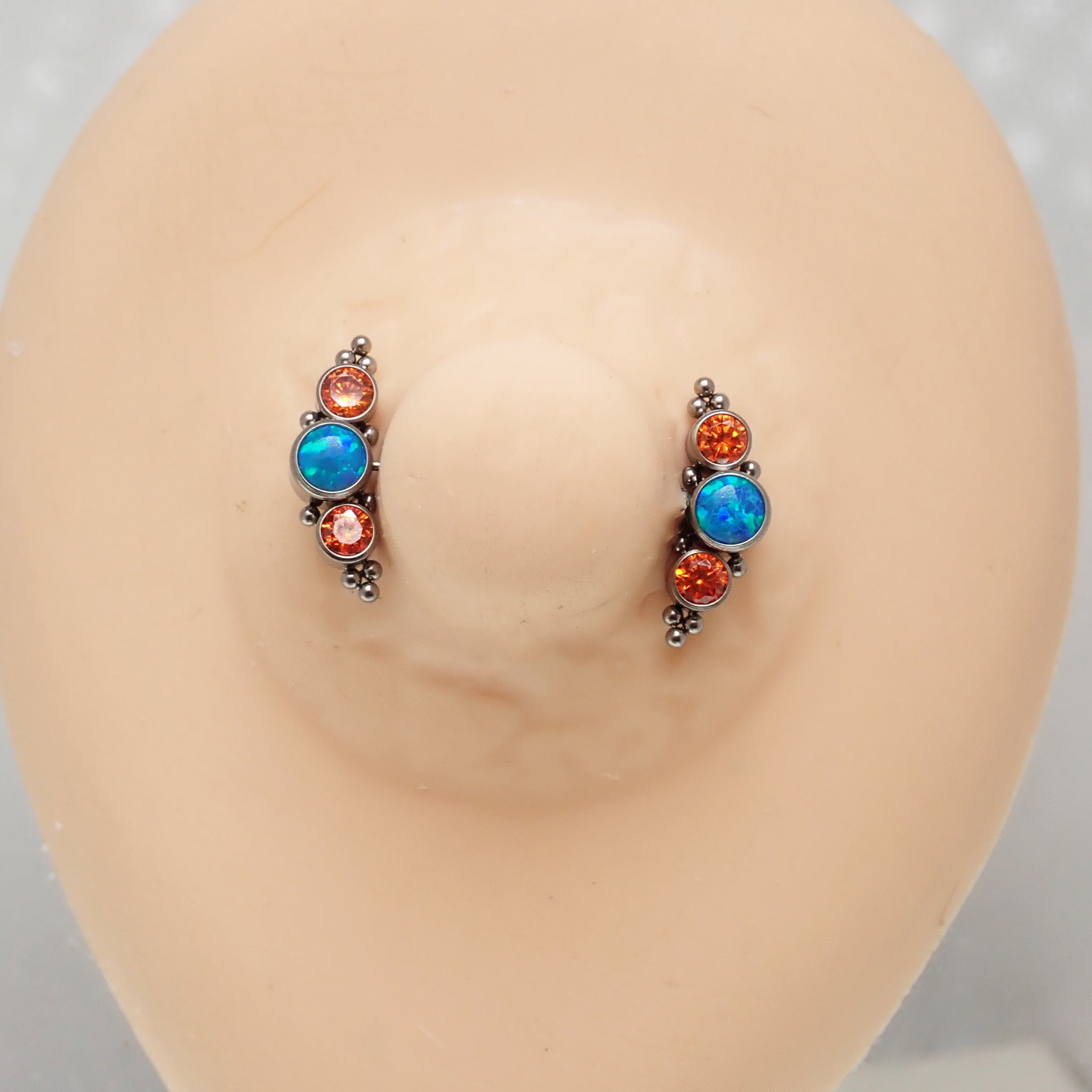 Teal opal and orange CZ push fit nipple bar in 14g body jewelry by Body Clickers, showing the colorful jewelry on a display.